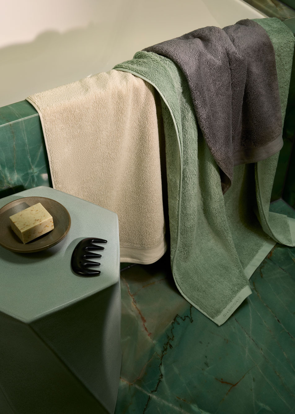 Several Sheridan bath towels draped over the side of a green marble bath tub