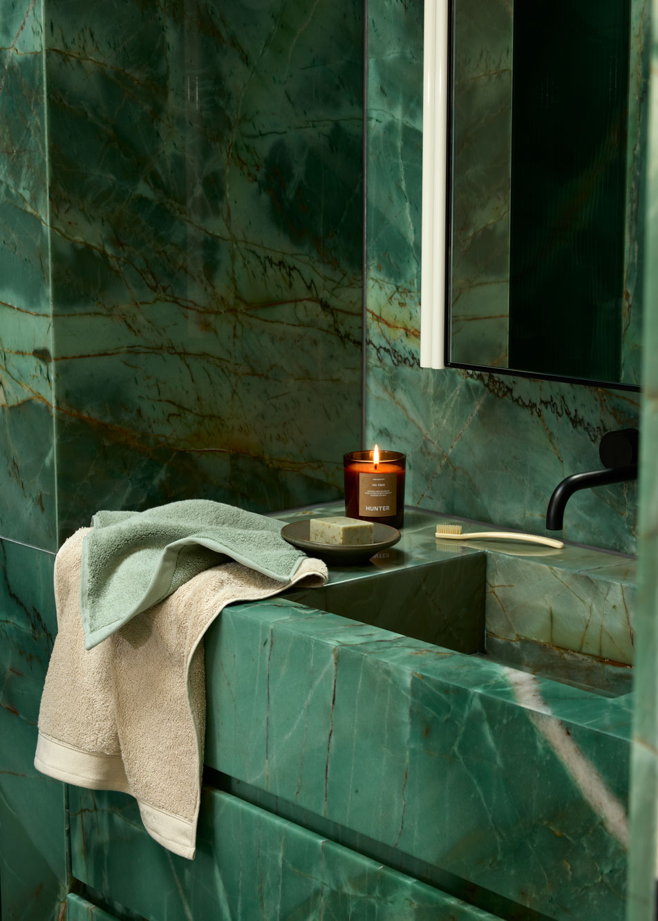 A candle and two Sheridan towels sitting on a green marble basin