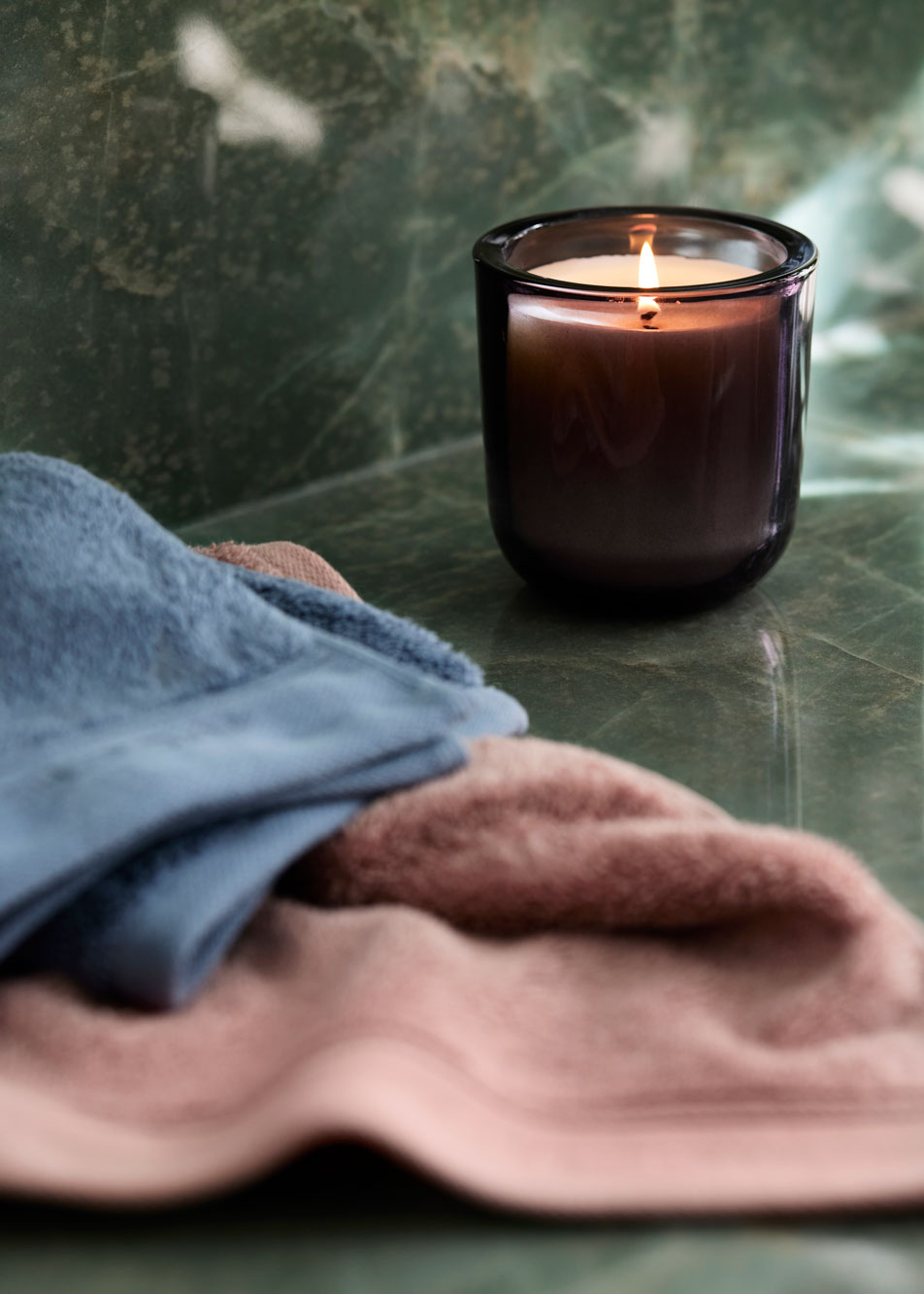 A lit candle and two bath towels sitting on top of a green marble counter top