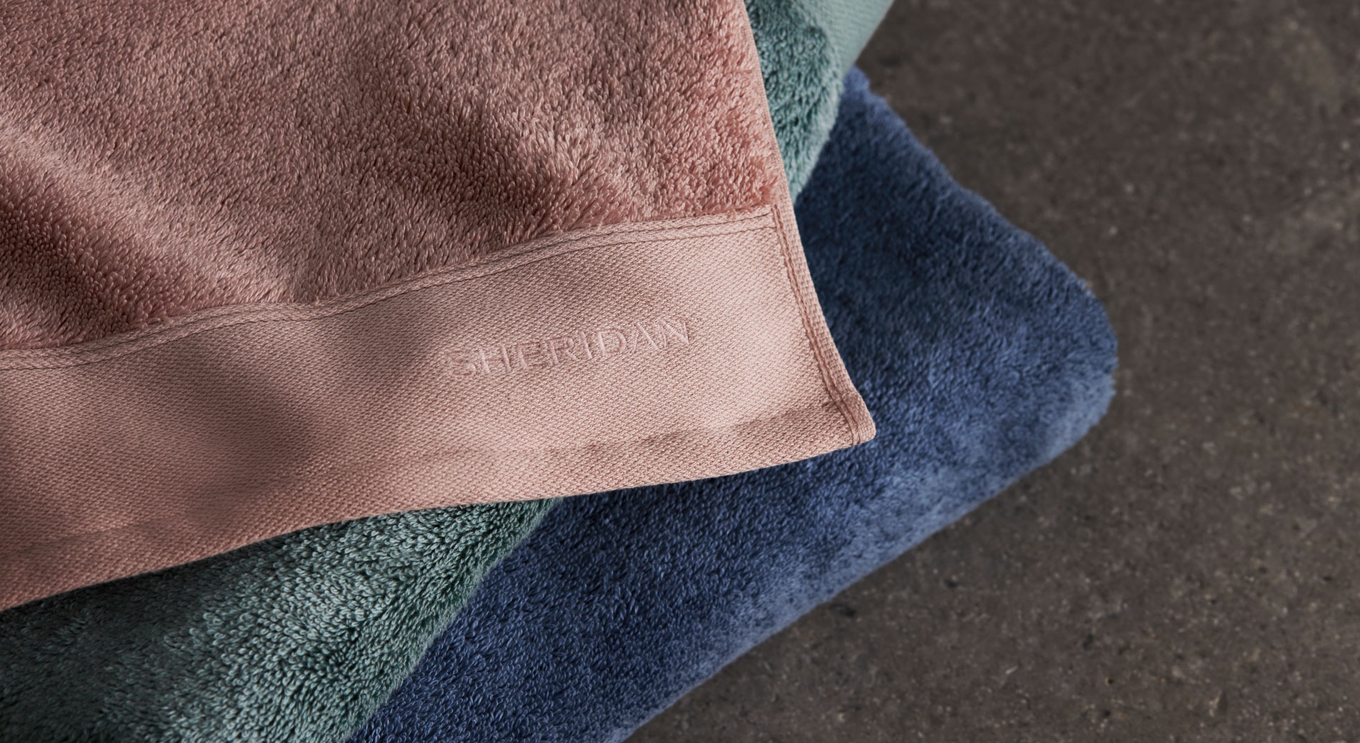 Sheridan Eris bath towels stacked on a concrete surface
