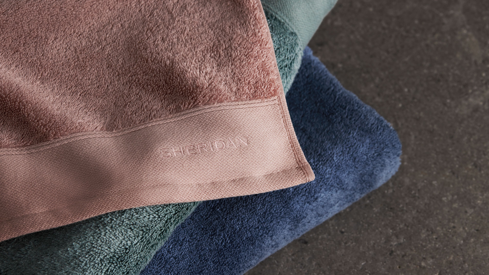 A stack of Sheridan Eris soft luxury towels folded on a grey granite benchtop