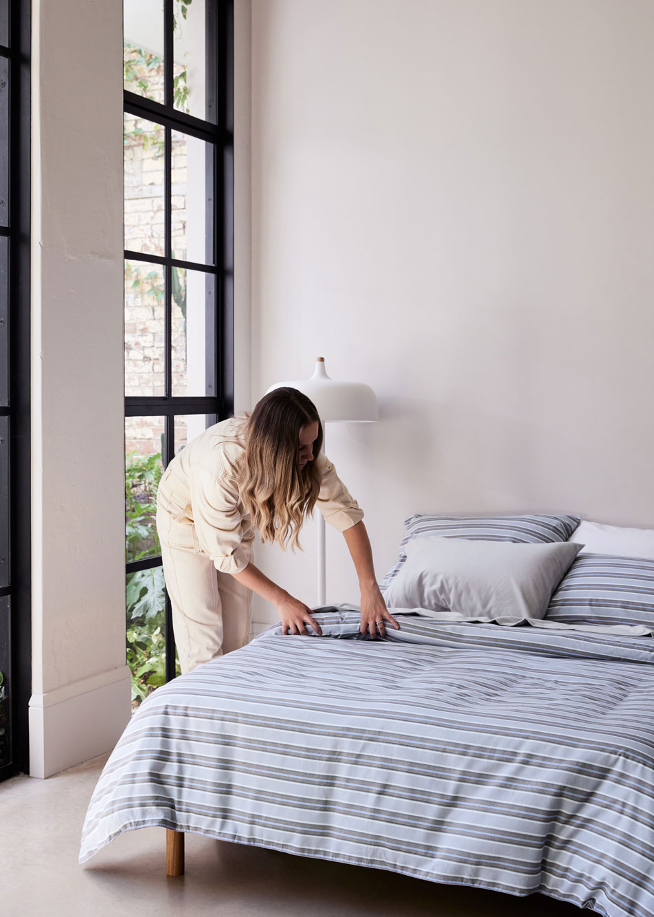 A young woman straightening a quilt cover on a bed