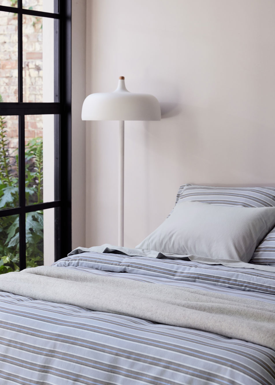 A bed dressed in flannelette bedding sits next to a white lamp. In the background is a tall French window.