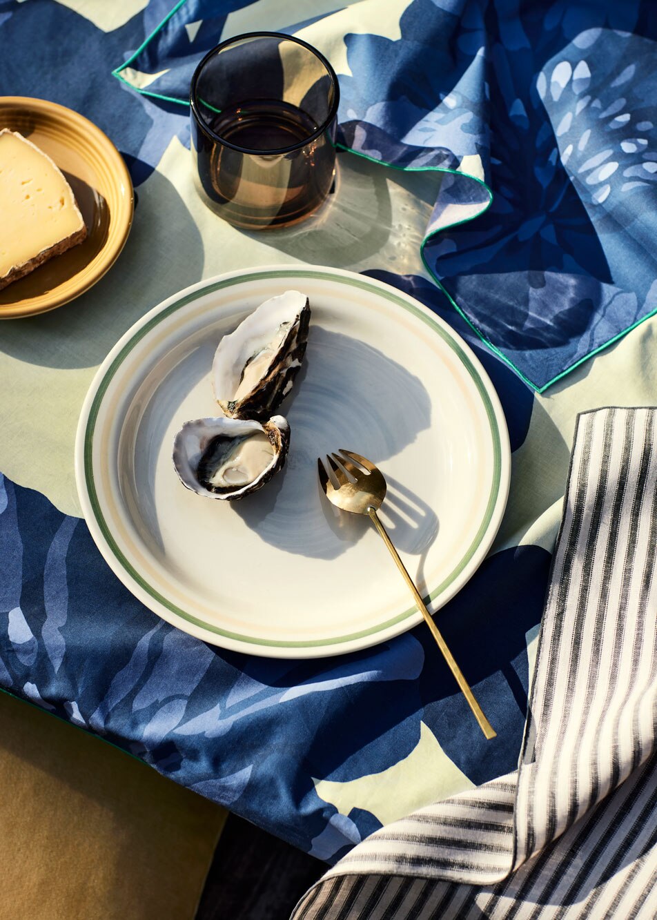 A close-up of a dining table dressed in a floral table cloth with striped linen napkins. A plate of oysters and a plate of cheese sit on top.