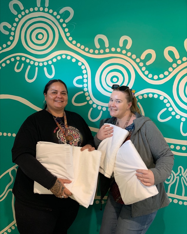 Two frontline homelessness workers standing in front of a painted wall holding SleepSafe sleep kits