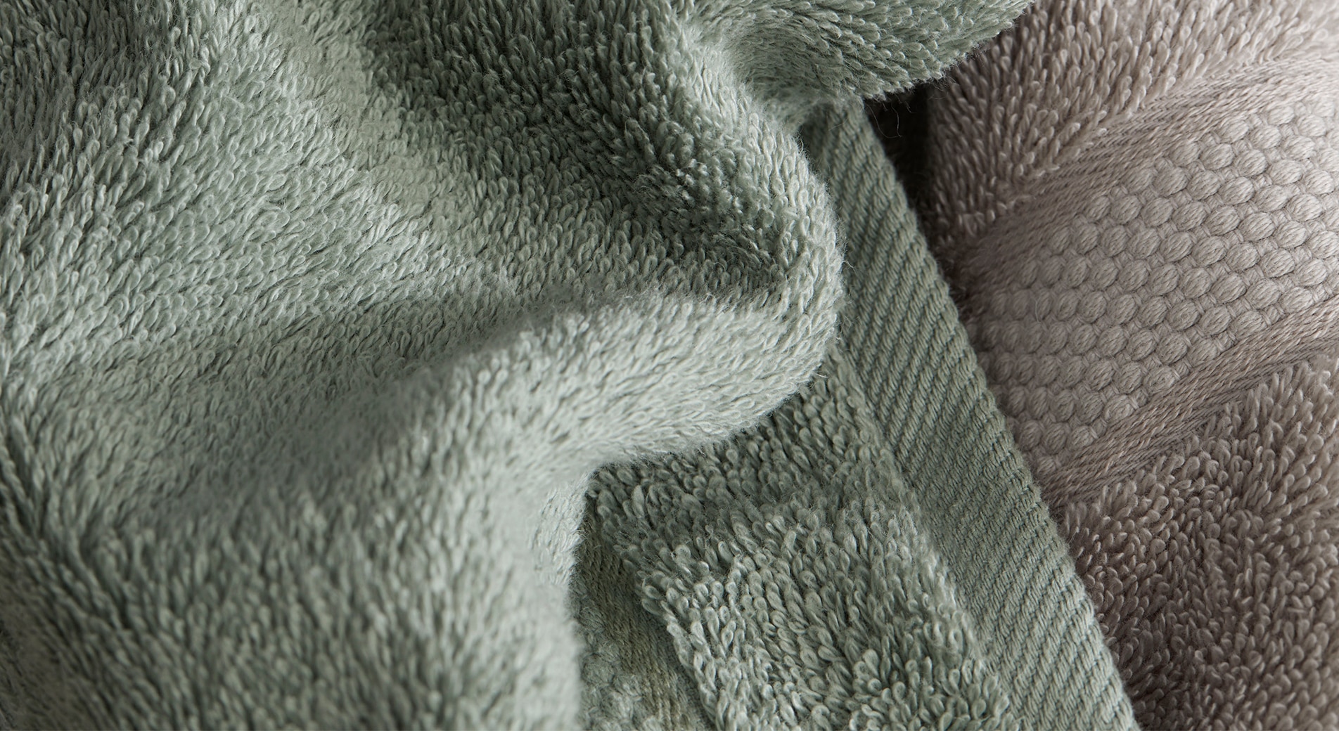 how do I make my guest bedroom luxurious? close up of luxury egyptian towel collection in dew green and slate grey, you can see texture and loop of towelling.