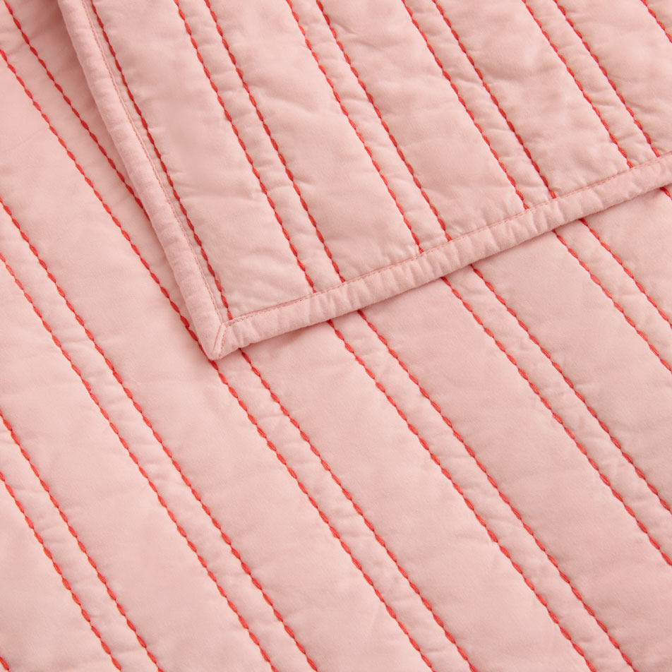 A close-up of a pink bed cover with red striped embroidery.