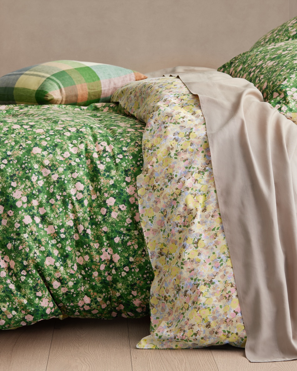 The side of a green floral bed, a plaid cushion sits on top