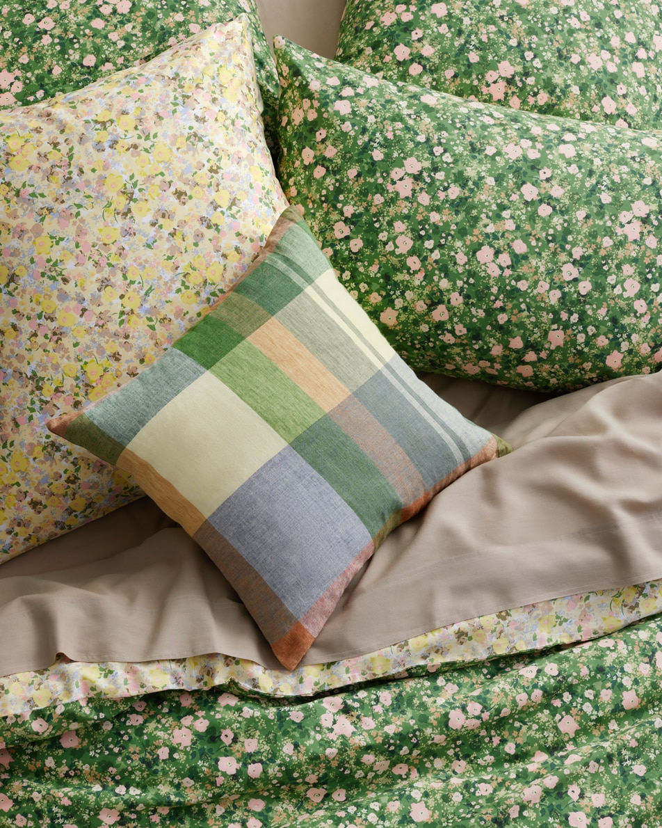 A plaid cushion on top of a green floral bed