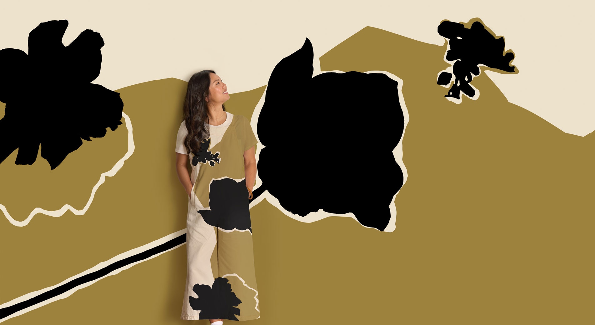 A woman stands, smiling in front of an abstract floral print background. Her jumpsuit is in the same matching pattern.