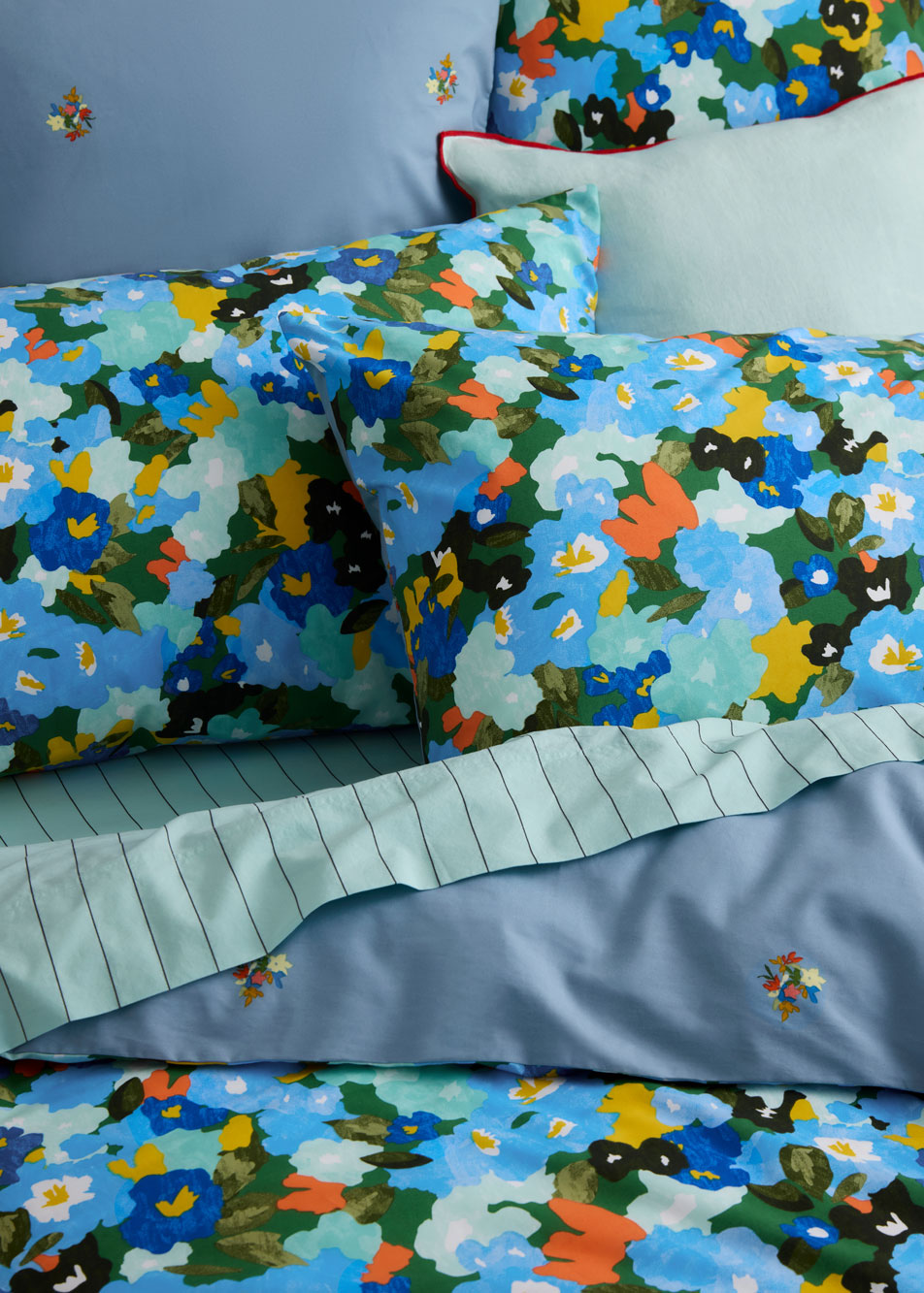 A close up of a bed dressed in bright floral quilt cover and pillows, paired with a blue striped sheet