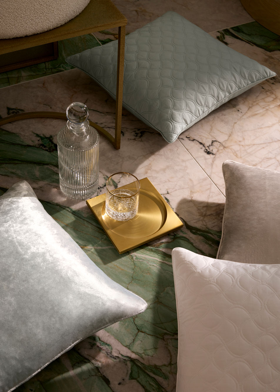 Four different cushions scattered on a marble floor with a golden dish and glass carafe