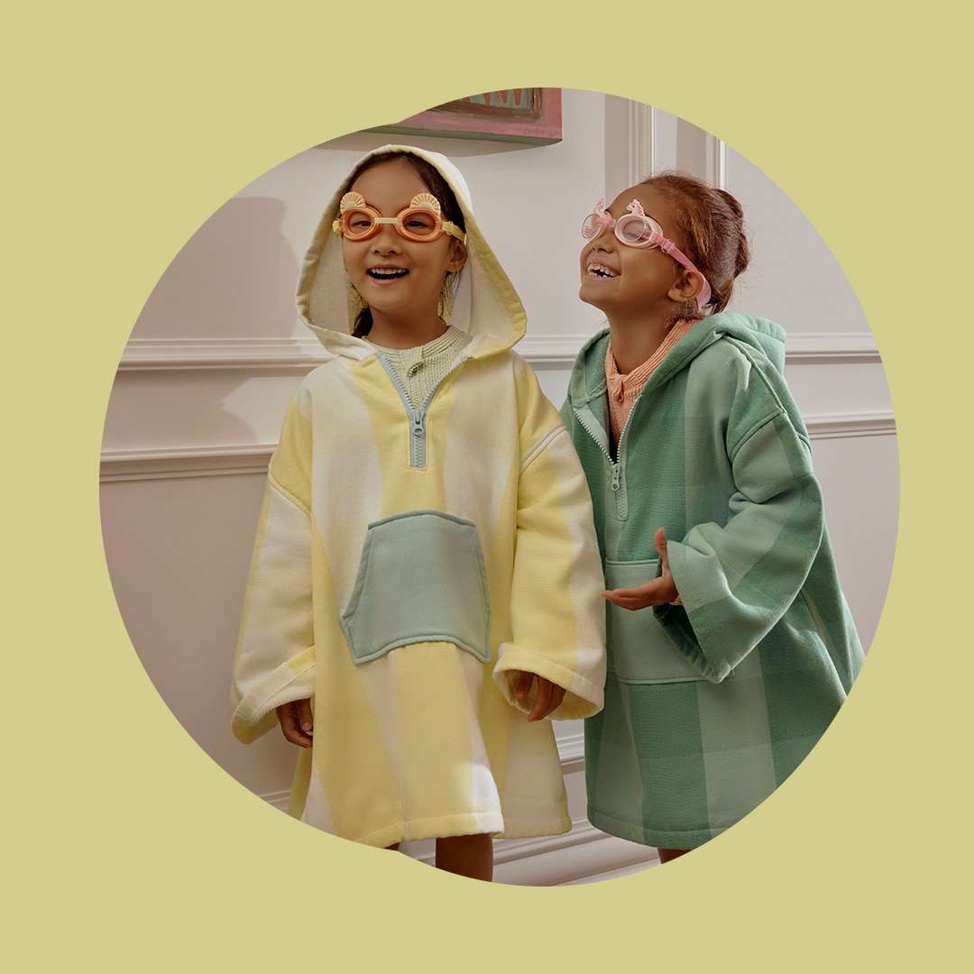 two little girls stand together, wearing ponchos with a check print. they are giggling to each other while wearing googles on their faces.