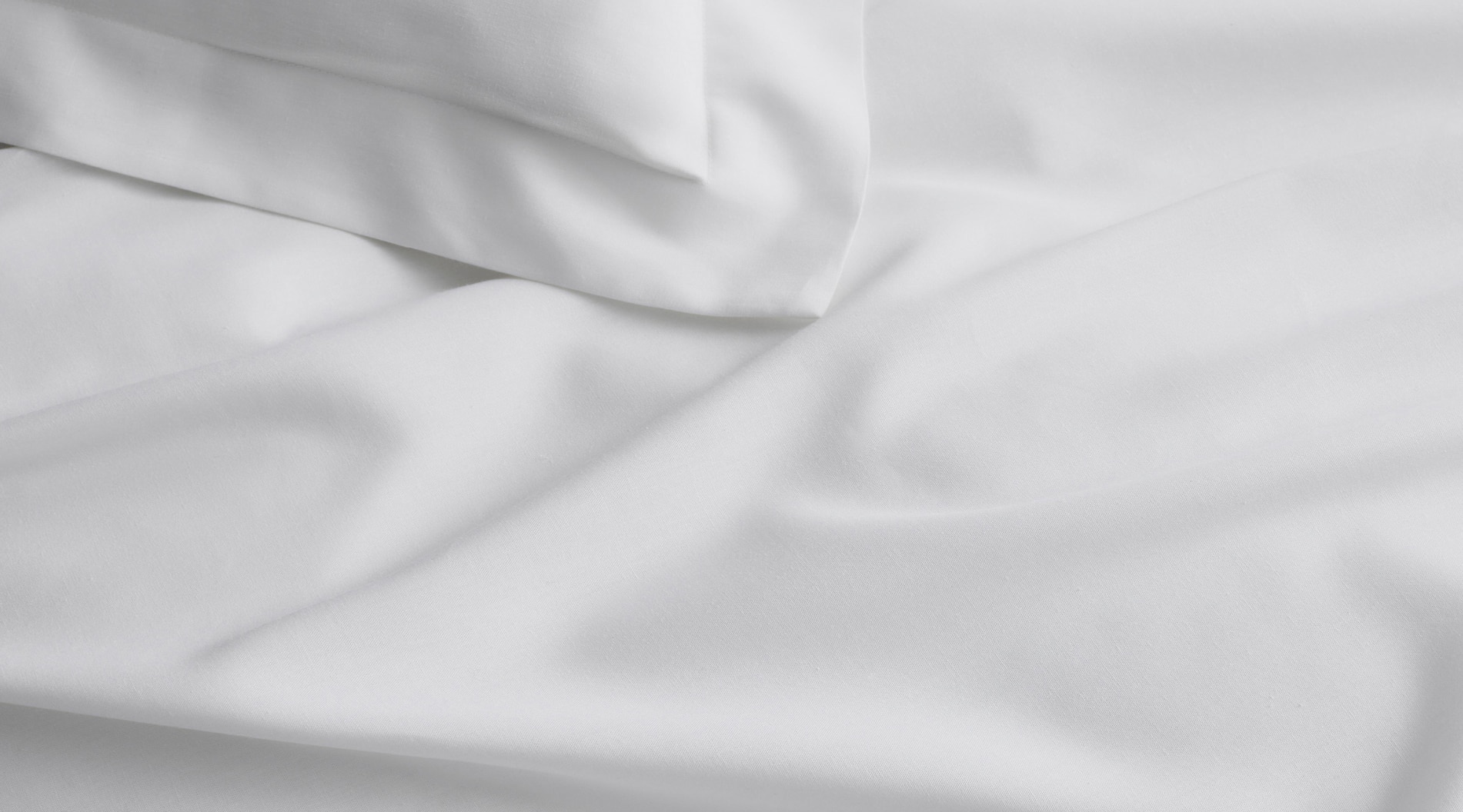 close up of belgian linen flax sheet and corner of pillow, in crisp white shade. detail shows how it drapes and crumples in a relaxed way.