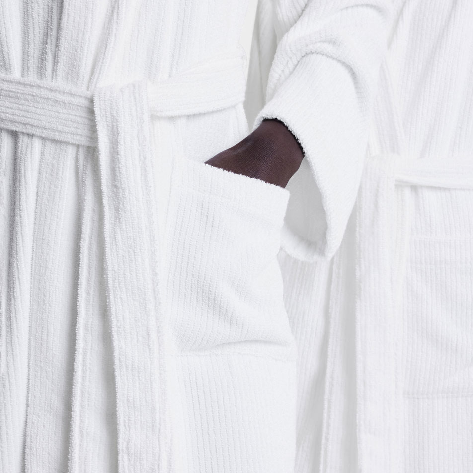 A close up image of someone wearing a white Living Textures robe, placing their hand in their pocket