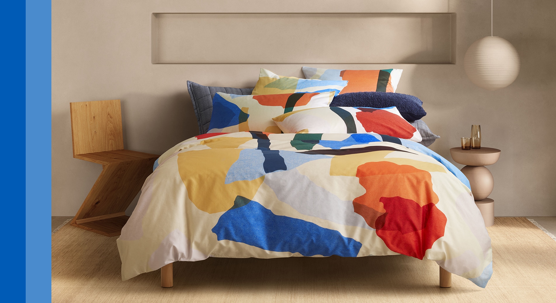 how to style a maximalist bed. image of multicoloured bed with abstract print, placed in a bedroom. two blue stripes are on the left hand side.