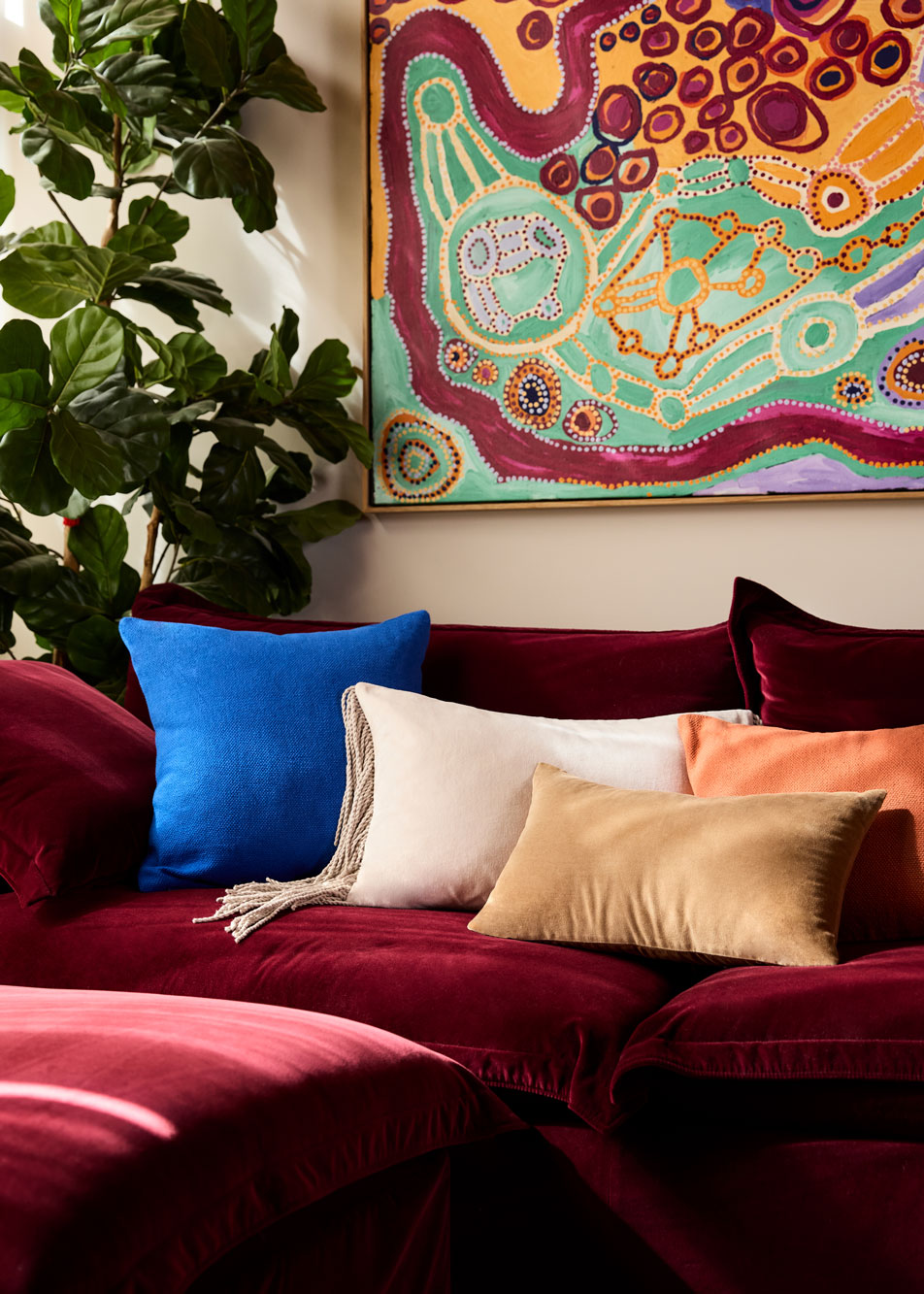 A modern, beige velvet sofa styled with a knit throw and two decorative cushions. In front of the sofa is a glass coffee table with a magazine on top.
