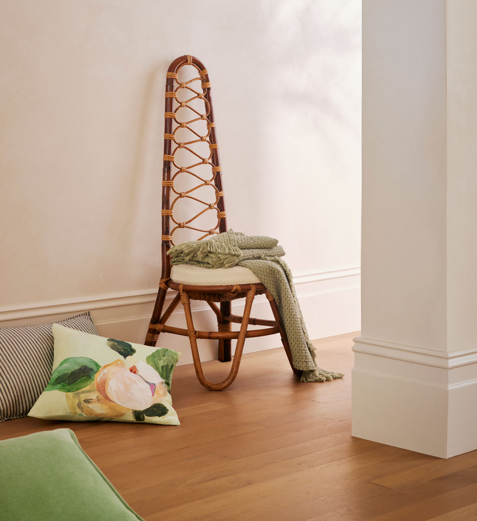 stripes and florals home decor. A wicker chair sits in a white hallway, draped with a green knit throw and various printed cushions scattered across the floor.