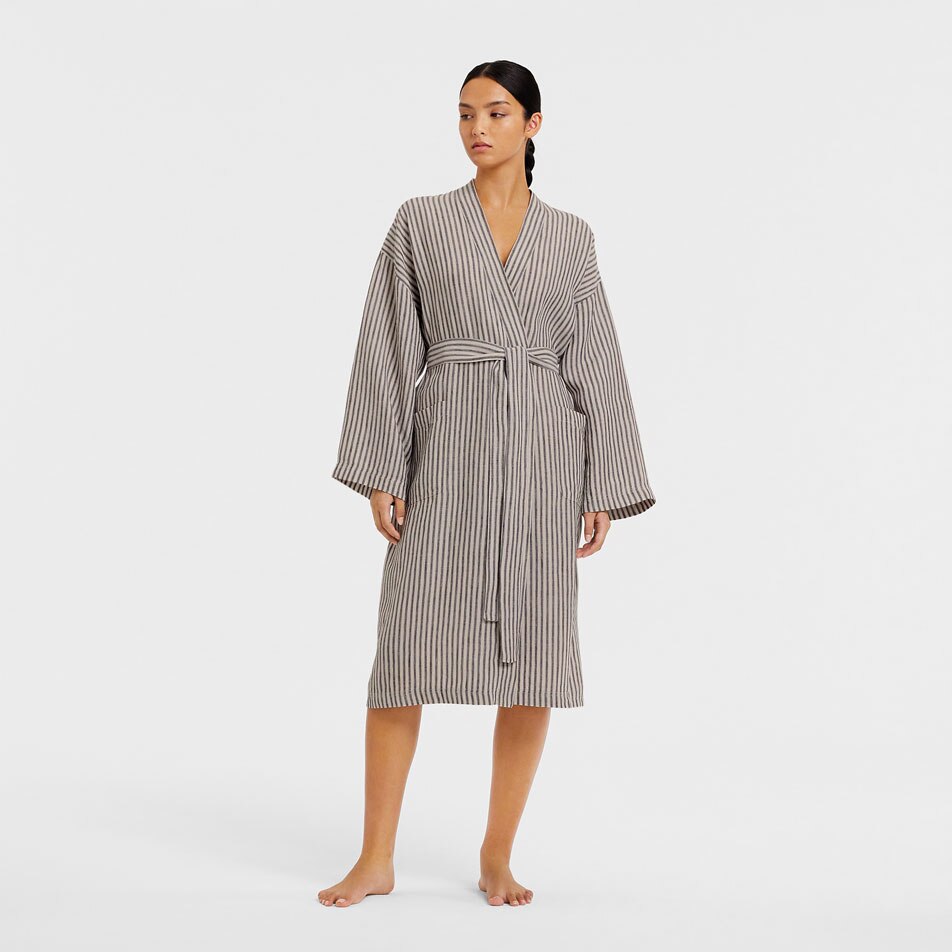 Brunette woman with a sleek ponytail models a grey striped linen robe in front of a white background