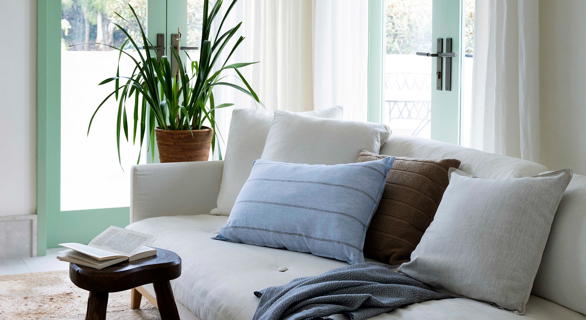 landscape shot of style living room. cream couch with blue blanket, blue striped cushion and brown and cream cushion. plant in background.