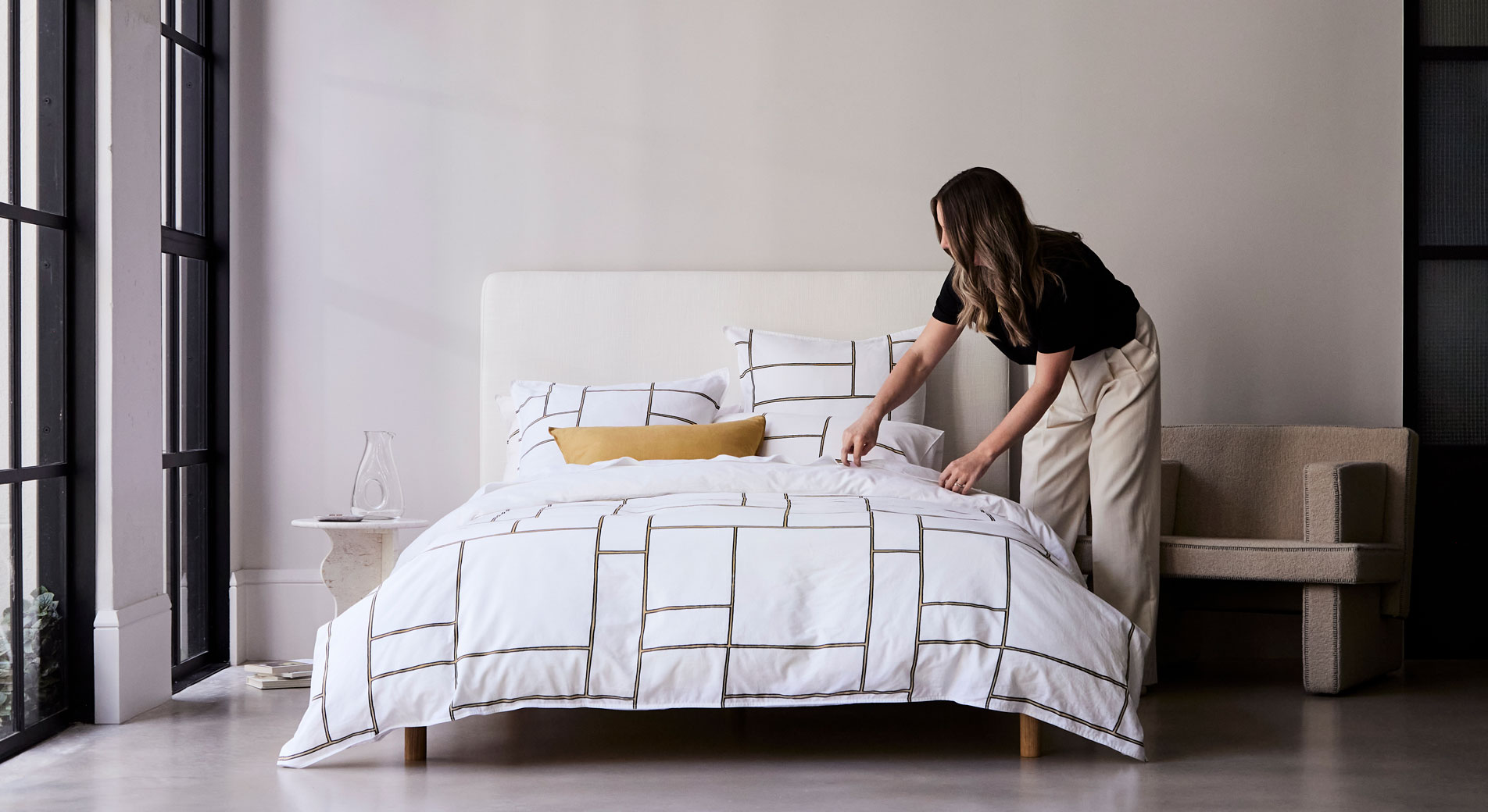 A woman making a bed with a geometric print quilt cover.