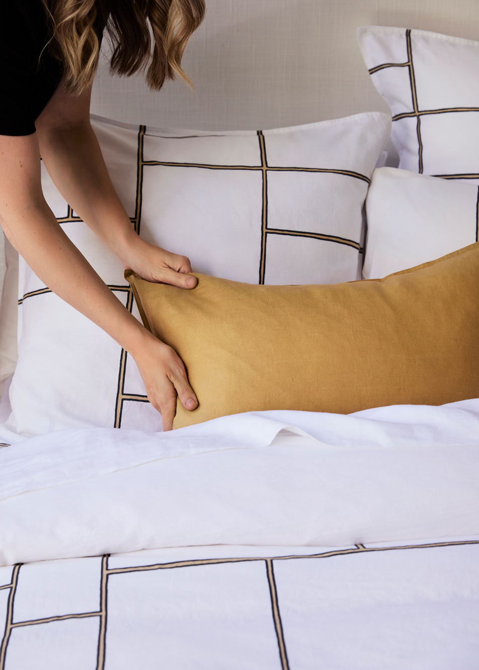 A woman straightening an accent cushion on a bed.