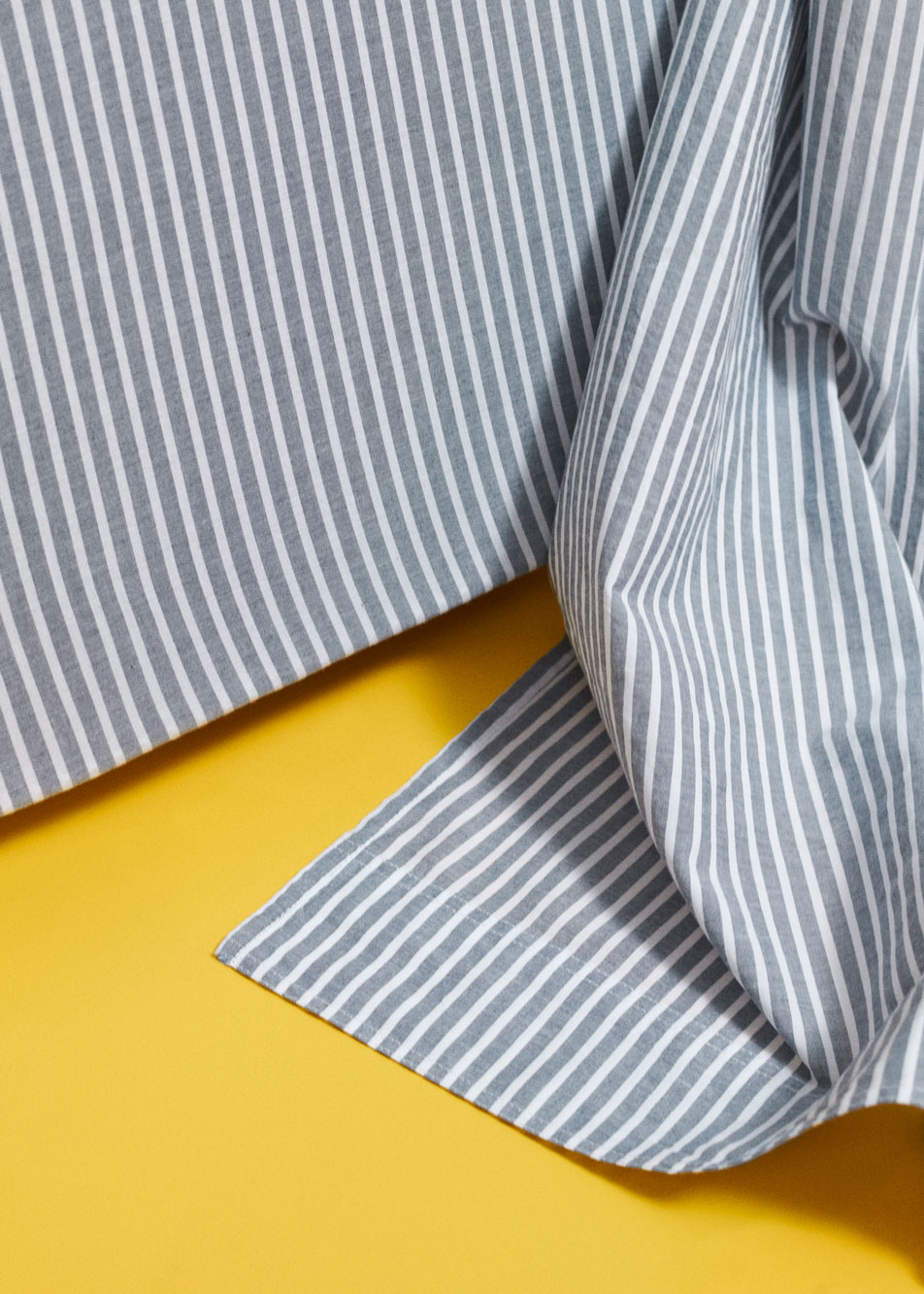 A blue and white striped sheet lying tousled on a bright yellow background