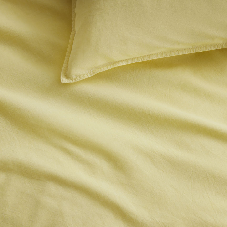 Close up photo of a Reilly chambray sheet set in yuzu. A matching pillow sits on top.
