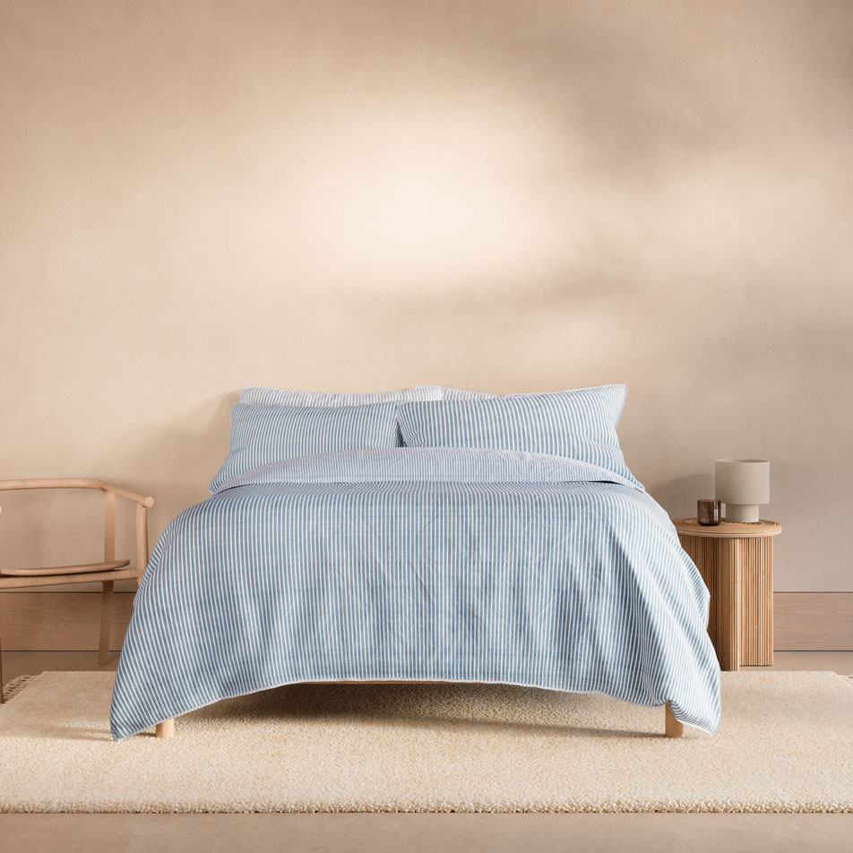 A bed with a Reilly Stripe Duo quilt cover in the colour chambray
