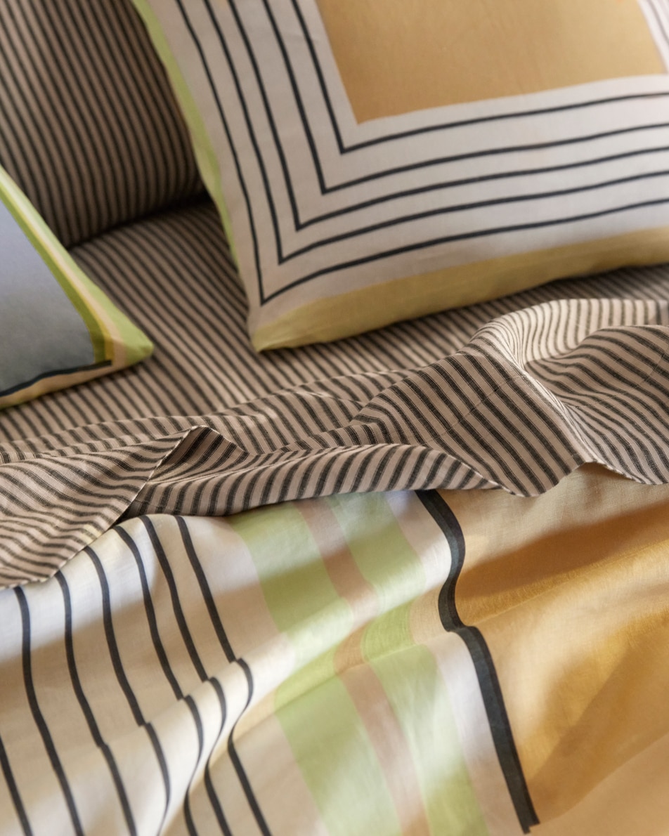 A close up image of striped linen sheets paired with colourful geometric linen bedding