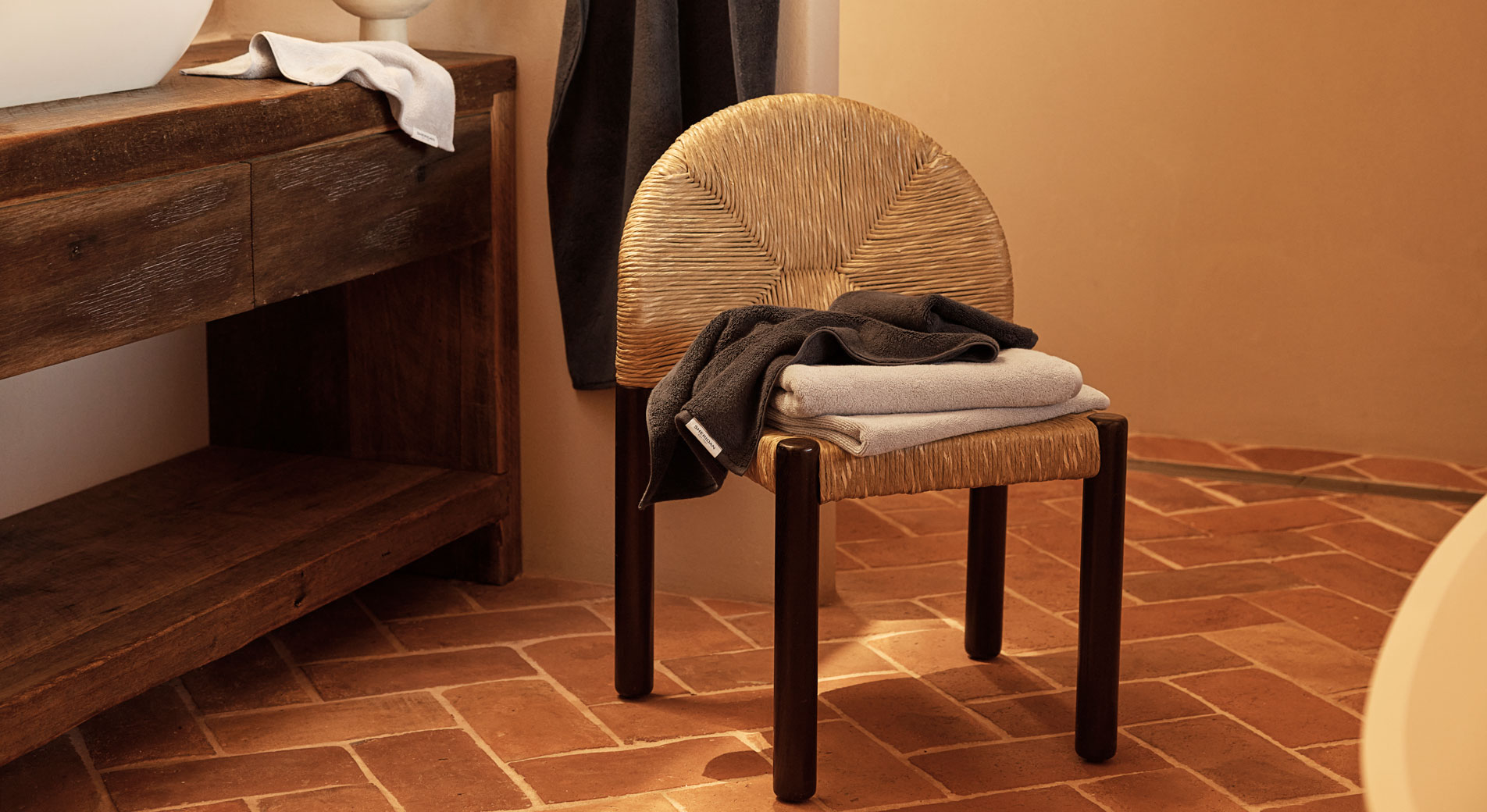 A wicker chair in the middle of a bathroom. On top is a stack of folded towels.