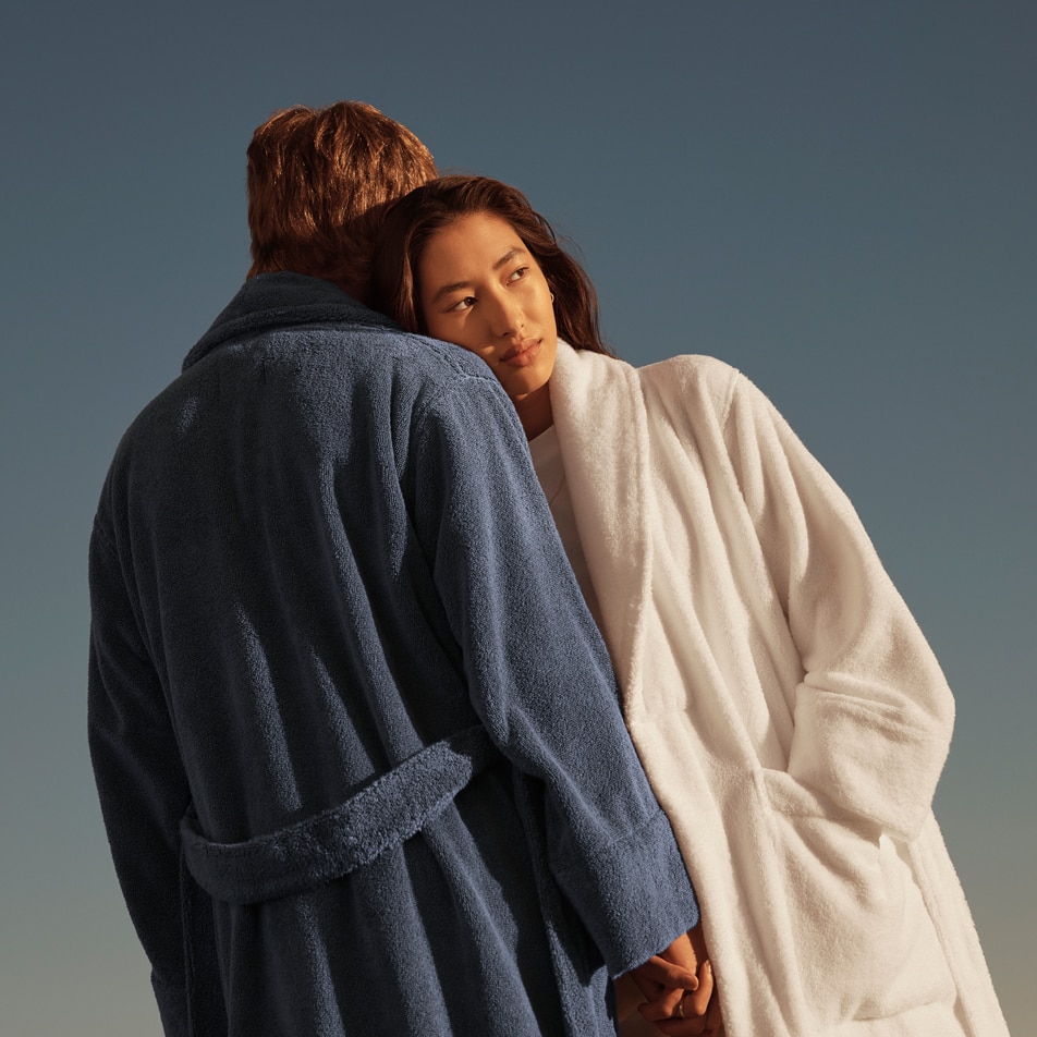 A woman leans on a man's shoulder, facing into the sun. Both are wearing Australian cotton terry bathrobes.