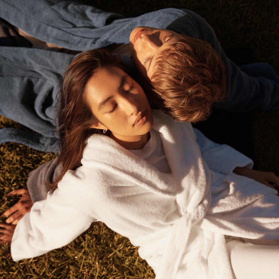 A young man and woman lay back on the grass, both wearing Australian cotton terry bathrobes