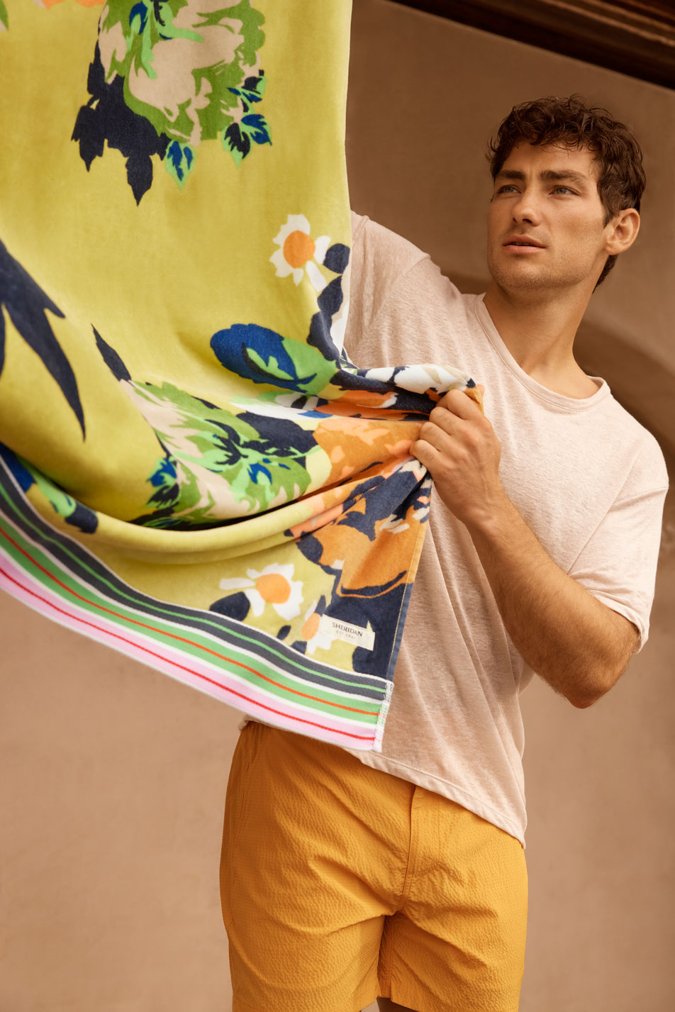 A young brunette man shaking out a bright floral beach towel