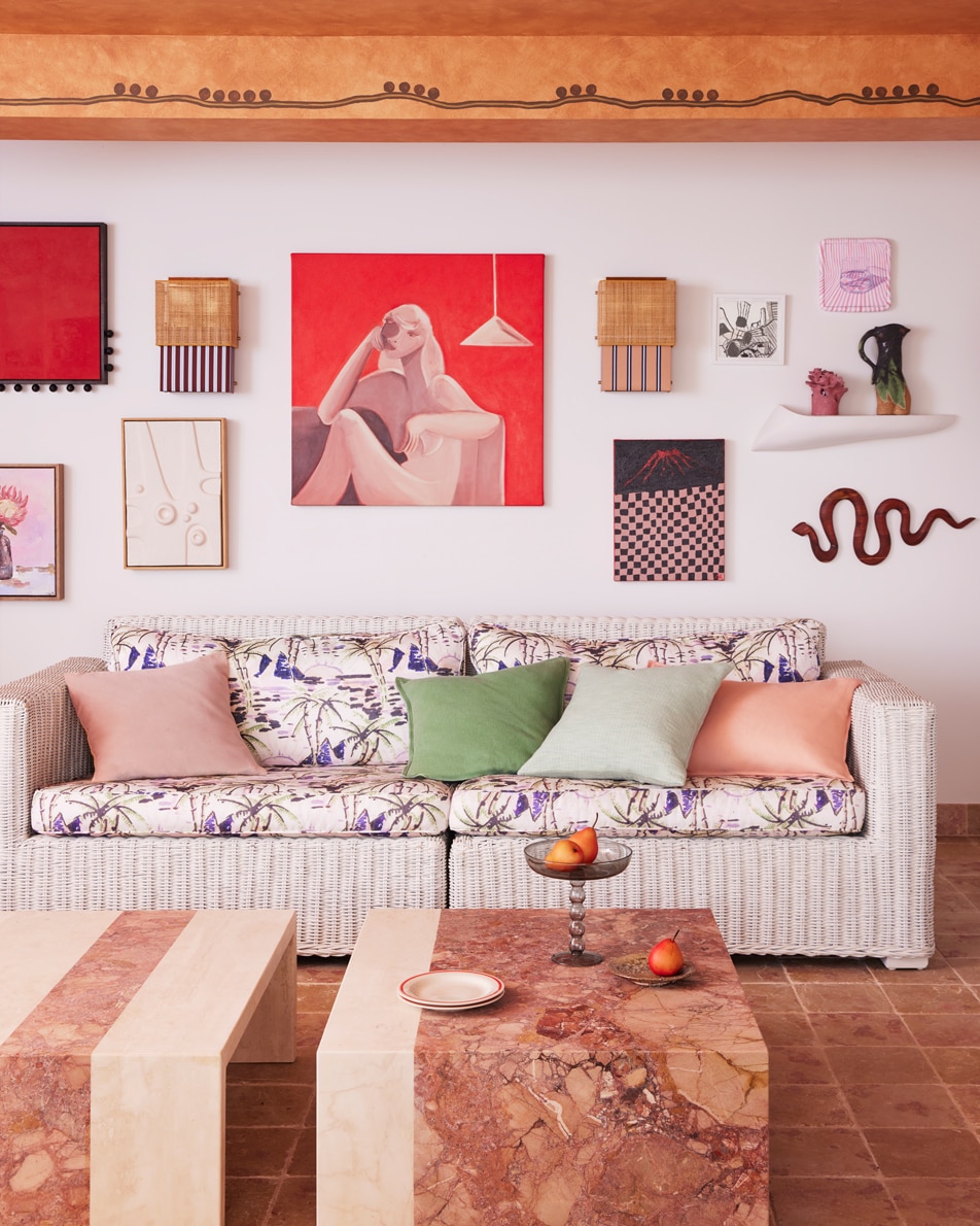 An eclectic living room with art on the walls, a lounge with multicoloured cushions and a pink marble coffee table