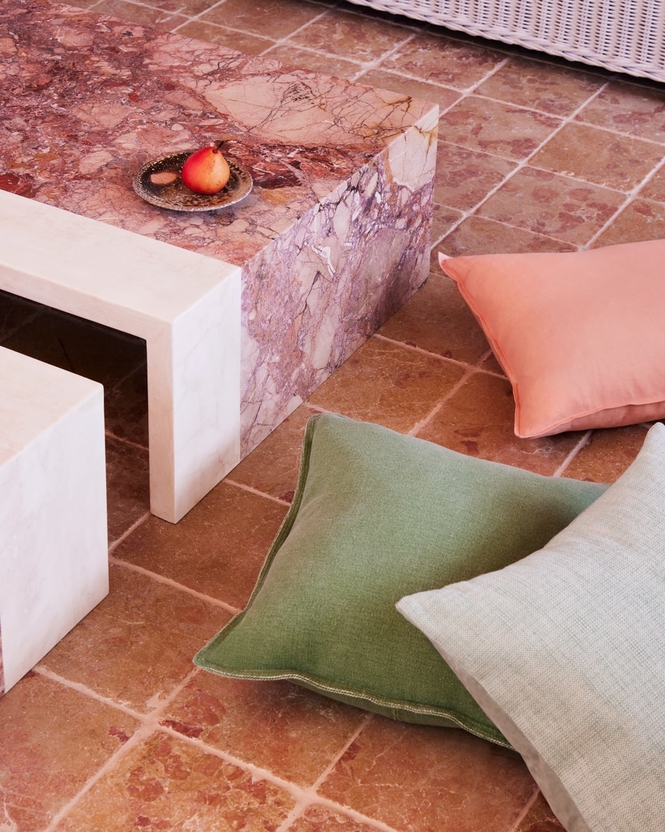 Cushions scattered on a tiled floor, next to a pink marble coffee table