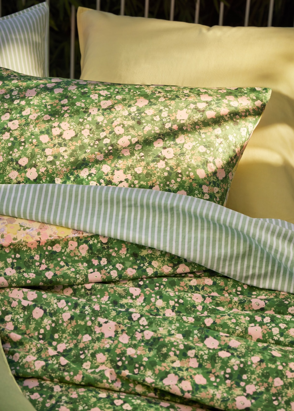 A close up image of a layered green bed with stripe and floral sheets
