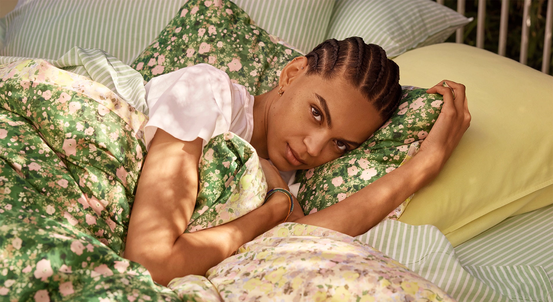 A young person laying in a plush green bed with floral and stripe bedding