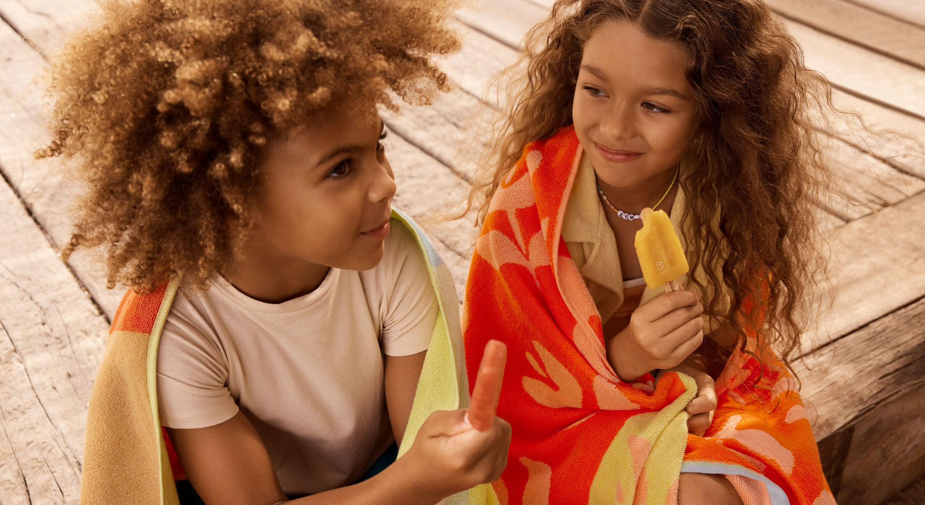 Two young kids with Sheridan beach towels wrapped around them, both holding ice blocks