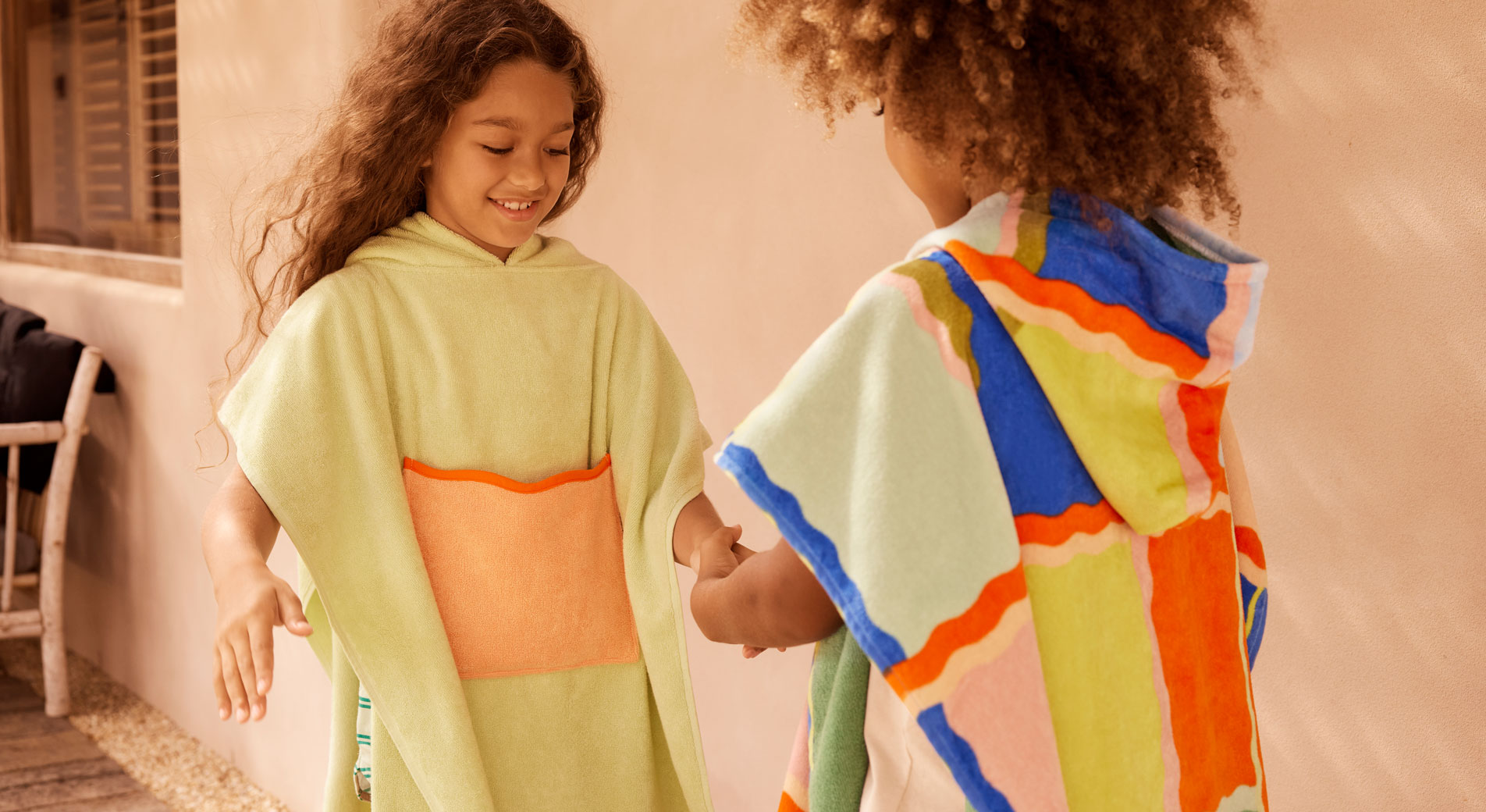 Two young kids wearing colourful Sheridan beach ponchos, playing a game
