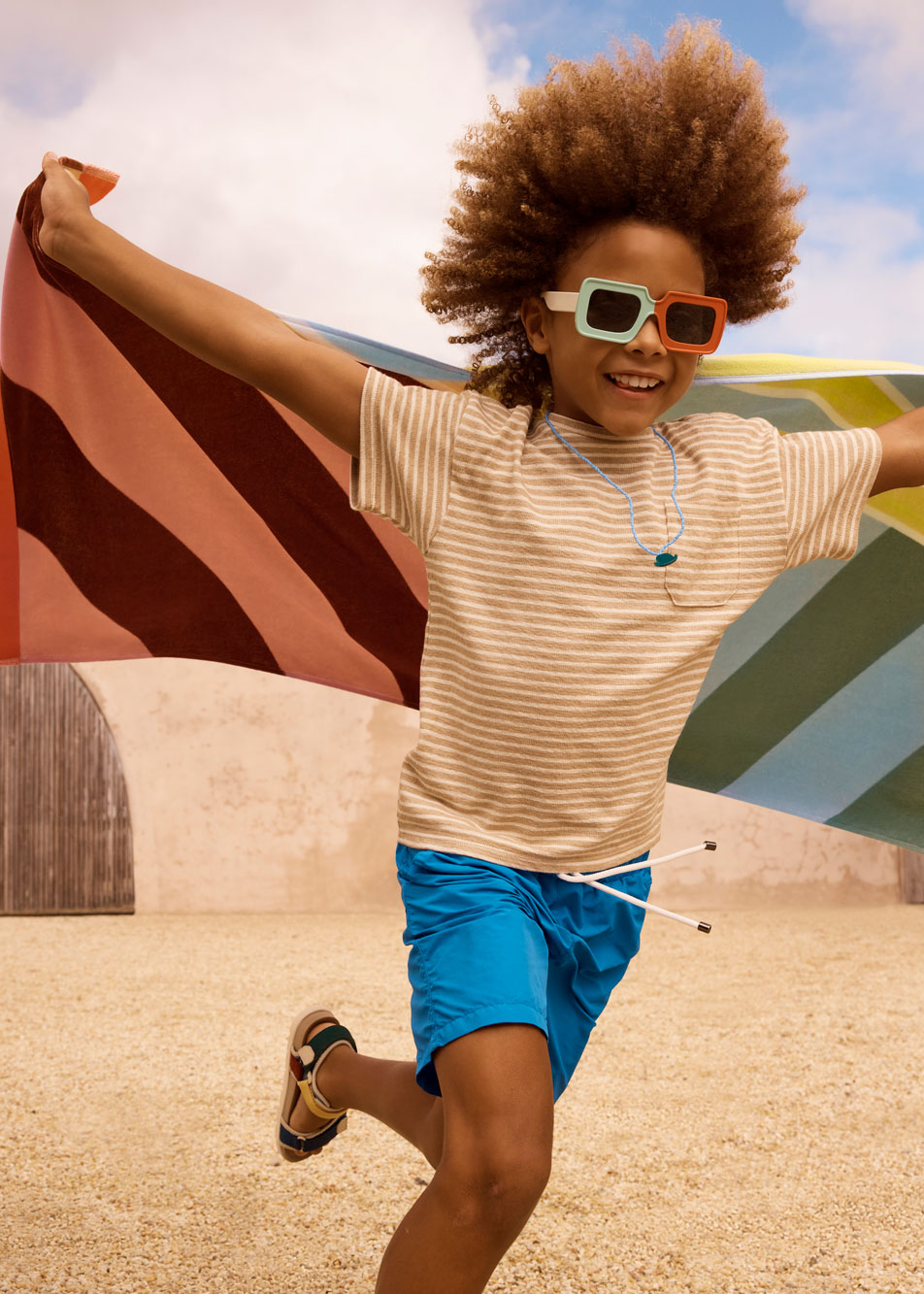 A young child running on the beach, holding a colourful striped towel