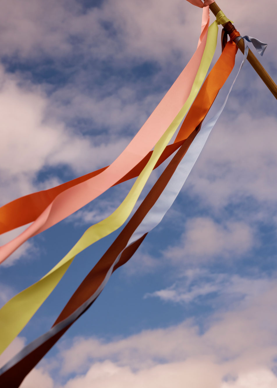 Colourful ribbons tied to a pole, blowing in the air with the sky in the background