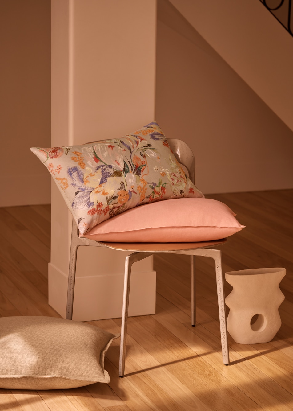 A floral cushion and a pink cushion sit on top of a chair in a room with a timber floor.