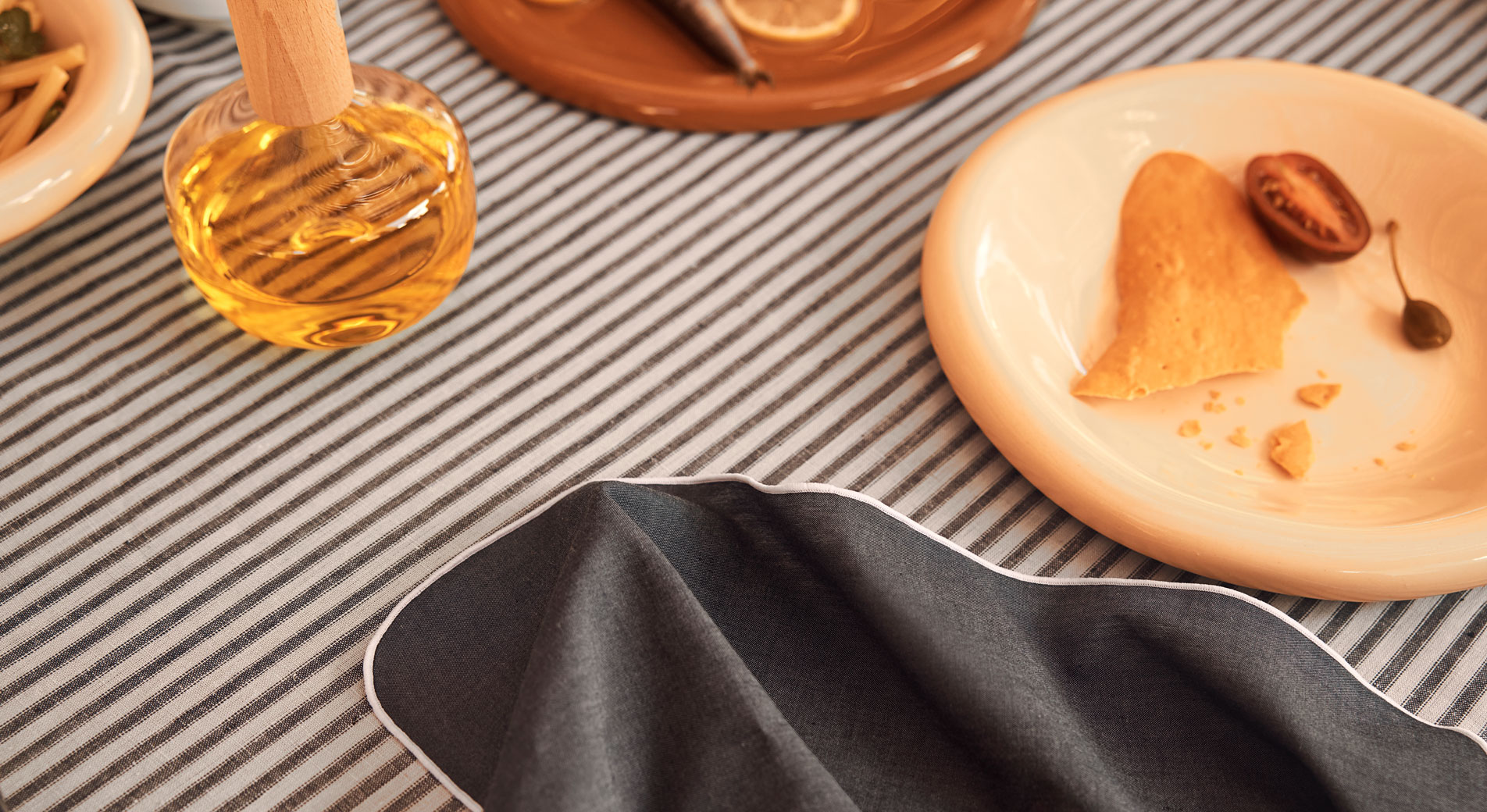 A table dressed with Sheridan table linen. Plates of food and a bottle of olive oil sit on top.