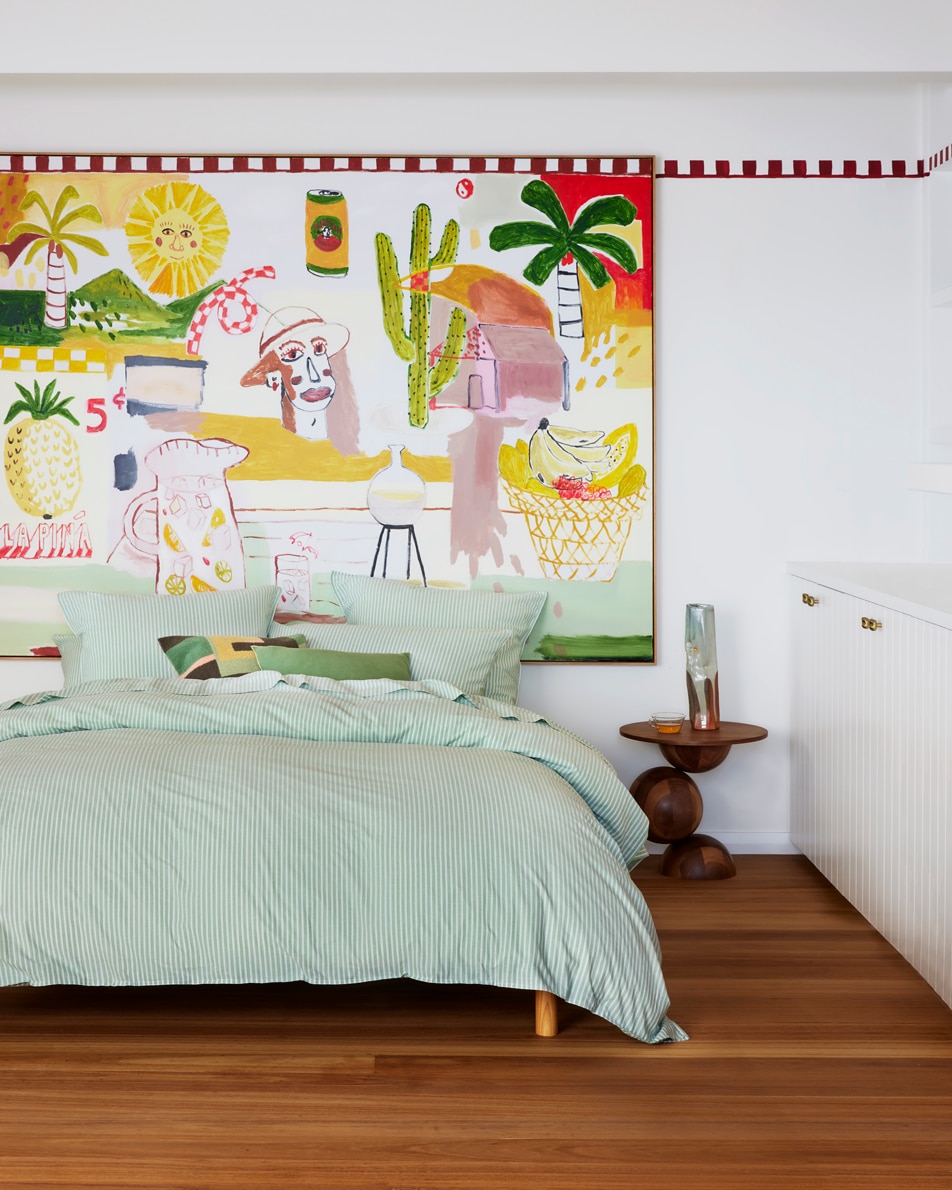 An image of a green striped bed sitting in a white bedroom. A large, colourful painted mural hangs on the wall.