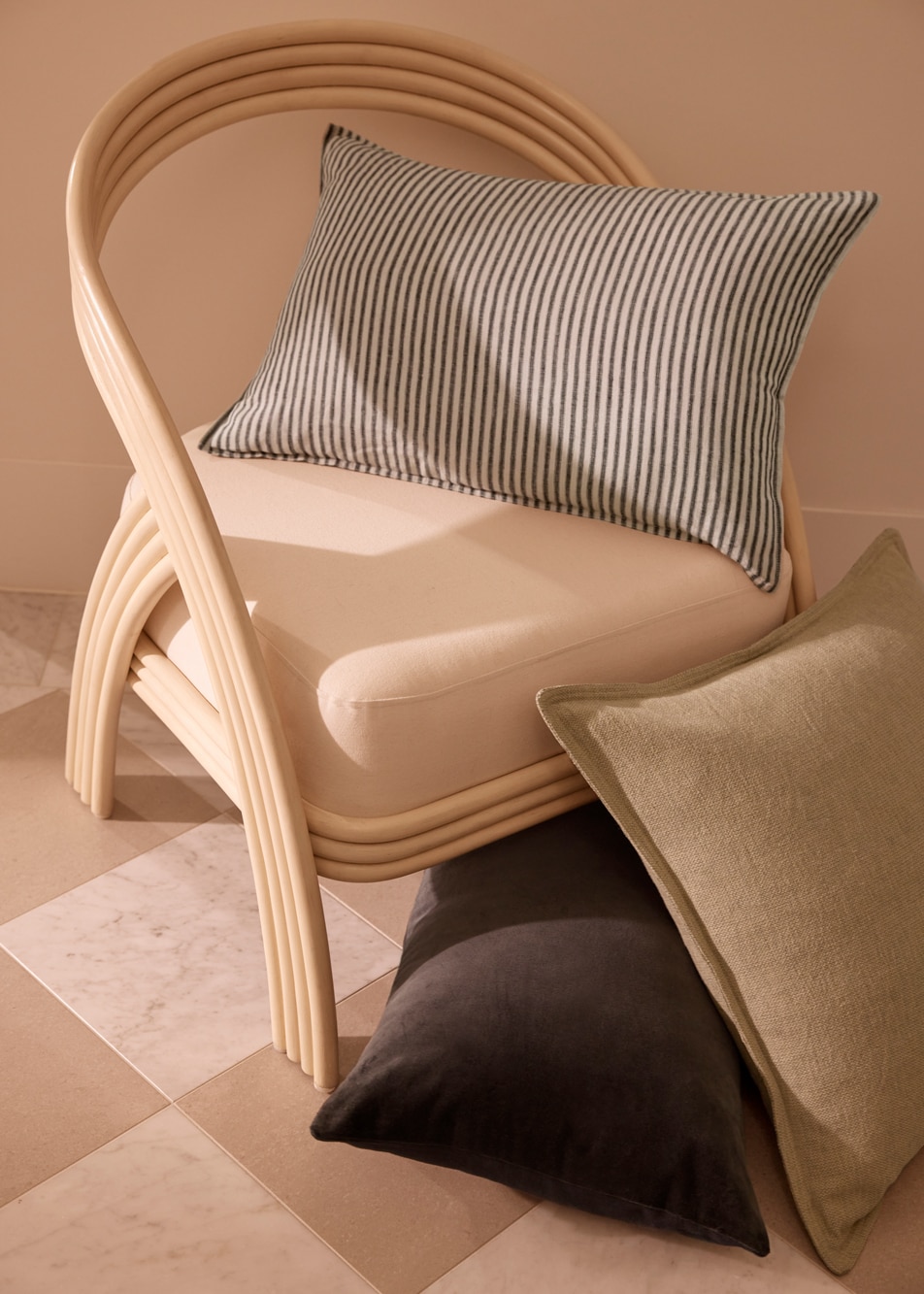 A stack of neutral coloured cushions on top of and next to a wooden chair