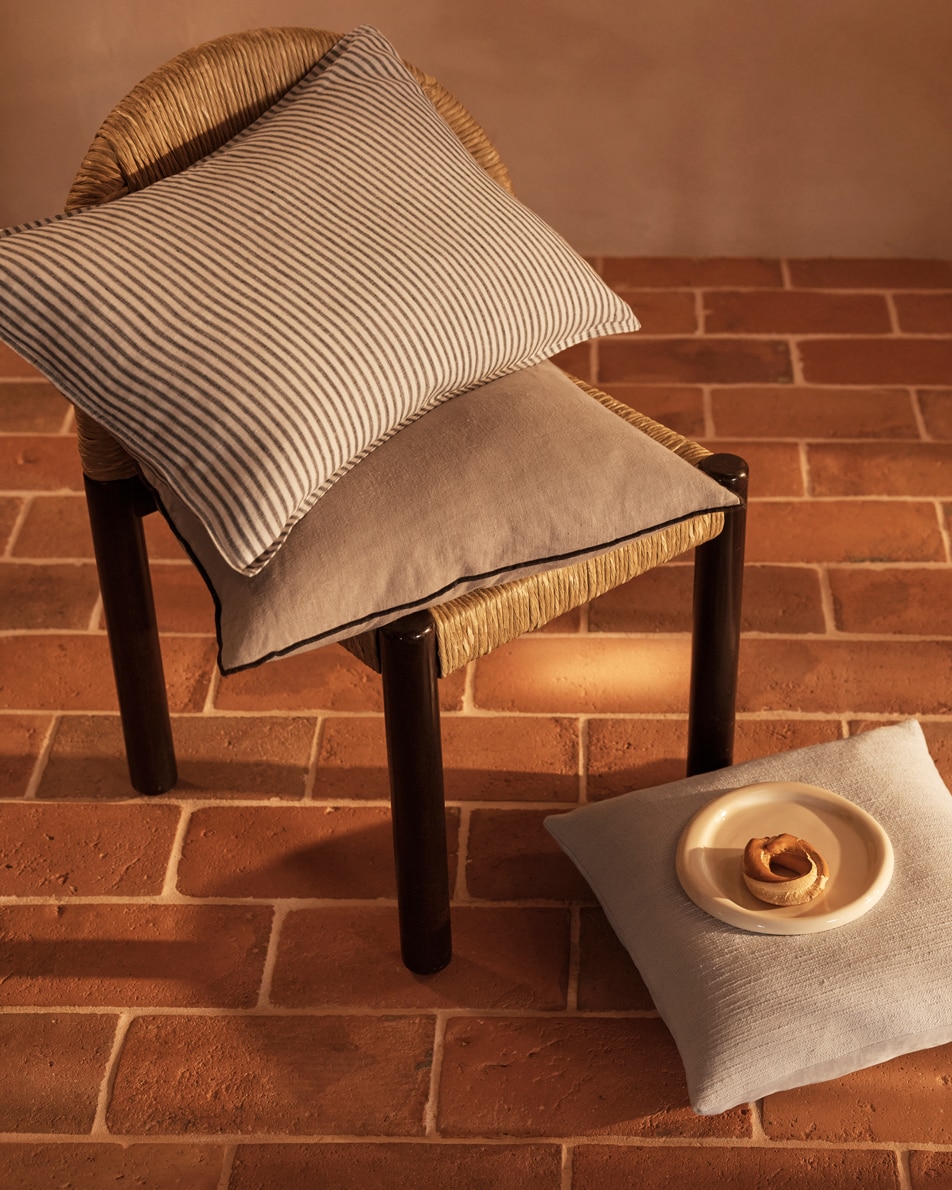 Two cushions sit on top of a chair. A third cushion sits on the floor with a plate and a pastry on top of it.