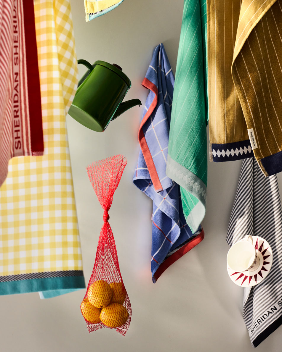 Sheridan tea towels in different colours are hung from the ceiling, alongside a green kettle and bag of oranges