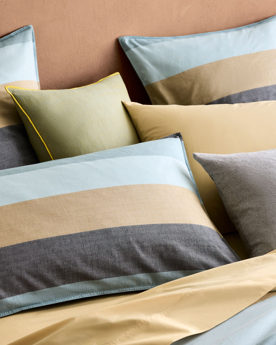 A close-up of a bed dressed in Reilly Club Stripe bedding in the colour blue grass.