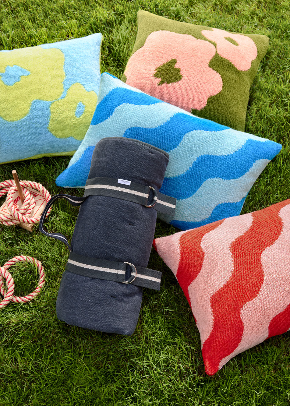 Assorted outdoor cushions and a picnic rug laying on grass